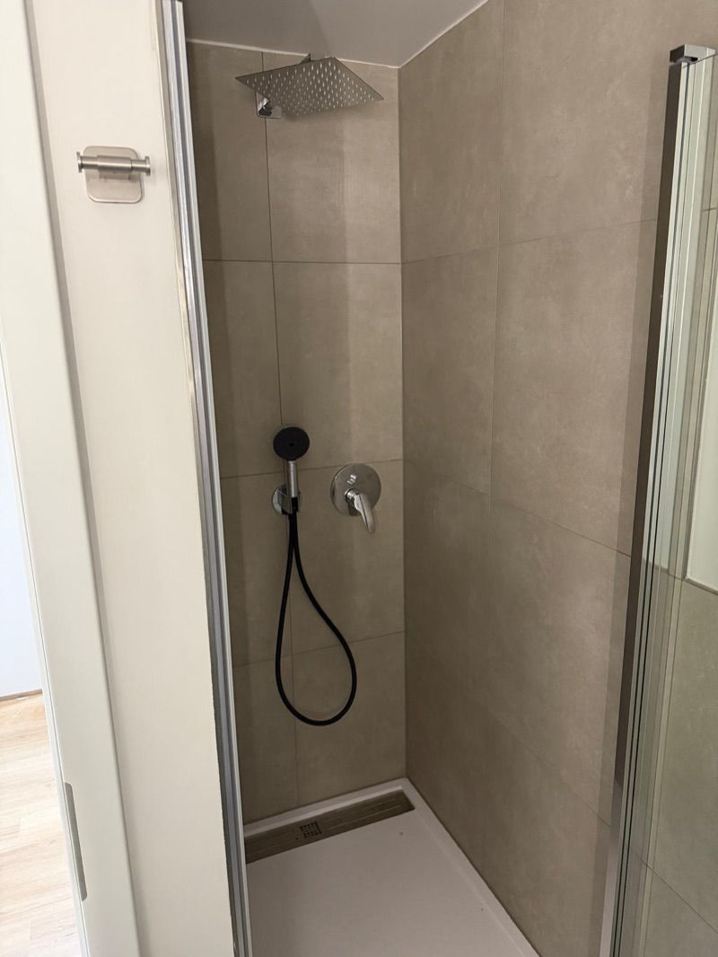 Dusche mit beigen Großformatfliesen, Regenbrause, Handbrause und flacher Duschwanne mit Rinne