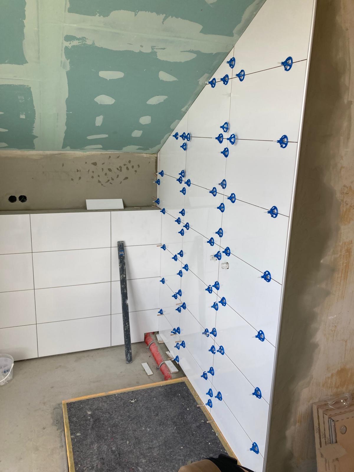 Großformatige weiße Wandfliesen unter einer Dachschräge, noch mit blauen Nivellierclips