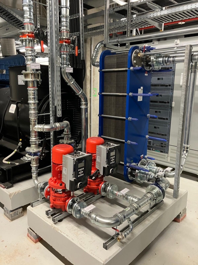 Blauer Plattenwärmetauscher mit zwei roten Umwälzpumpen auf einem Betonsockel in einer Technikzentrale