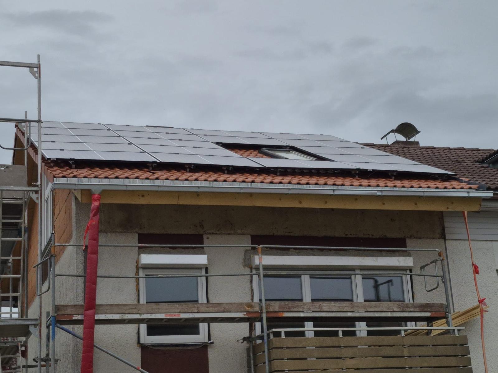 Photovoltaikmodule auf dem Ziegeldach eines Wohnhauses, darunter das Gerüst an der Fassade